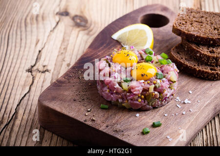 Steak Tartar in Ring-Form geformt, gekrönt mit zwei Wachteln Eigelb und mit Roggenbrot auf Holzbrett serviert Stockfoto