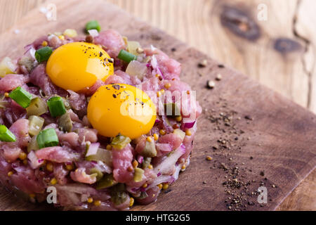 Steak Tartar in Ring-Form geformt, gekrönt mit zwei Wachteln Eigelb und mit Roggenbrot auf Holzbrett serviert Stockfoto