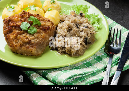 Gebratenes Schweinefleisch Schnitzel serviert mit gekochten Kartoffeln und gebratene Sauerkraut auf einem Teller Stockfoto