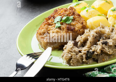 Gebratenes Schweinefleisch Schnitzel serviert mit gekochten Kartoffeln und gebratene Sauerkraut auf einem Teller Stockfoto