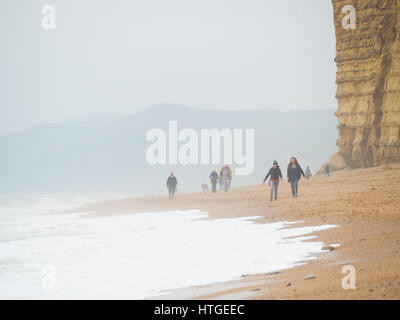 Burton Bradstock, Dorset, UK, 11. März 2017, Menschen am Strand Burton Bradstock Strand spazieren an einem dunstigen und nebligen Tag im West Dorset St Burton Bradstock Strand, Dorset, UK. © Dan Tucker/Alamy Live-Nachrichten Stockfoto