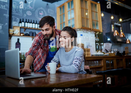 Junges Paar in einem Café-Restaurant mit Laptop am Tisch lächelnd. Stockfoto