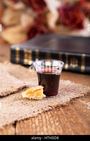 Die Kommunion. Tasse aus Glas mit Rotwein, Brot und Bibel auf Holztisch Nahaufnahme Stockfoto