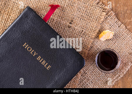 Die Kommunion. Tasse aus Glas mit Rotwein, Brot und Bibel auf Holztisch Nahaufnahme Stockfoto