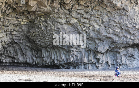 Ein kleines Kind schaut klein im Vergleich zu hoch Basalt Felsen und große Höhle bei Reynisfjara, Island, im Winter Stockfoto