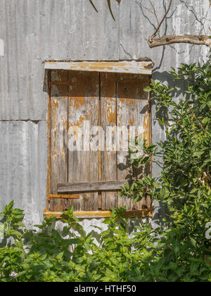 Abgenutzte shuttered Fenster auf einer Wellpappe Zinn vergossen Stockfoto