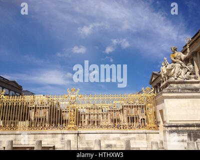 Gold Eingangstore zum Schloss Versailles bei Paris, France.Deep blauer Himmel, schimmert in der Sonne gold Tor. Steinstatue von La Paix (Friede) b