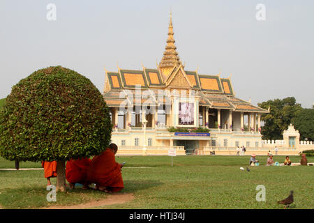 Ein buddhistischer Mönch überprüft sein Handy während der Zuflucht im Schatten eines Busches, vor dem Königspalast in Phnom Penh, Kambodscha. Stockfoto