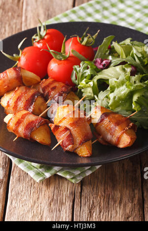 Gegrillte Kartoffelscheiben mit Speck und frischem Salat Nahaufnahme auf einer Platte. vertikale Stockfoto