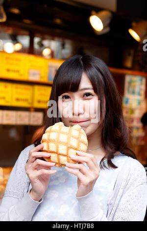 Modische Japanerin essen Brot in einer traditionellen Einkaufsstraße, Tokyo, Japan Stockfoto