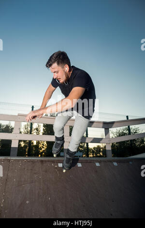 Kerl Rollerbladen und anhören von Musik im Kopfhörer im Freien. Siffer auf Rampe. Hohe Geschwindigkeit und gefährliche Tricks. Stockfoto