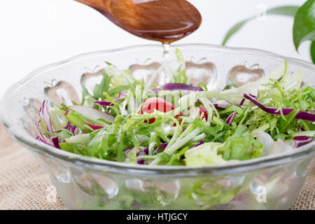 Gießen Öl in den Salat über einen Löffel, gesunde Ernährung Lebensstil. Frischer Salat mit Öl Stockfoto