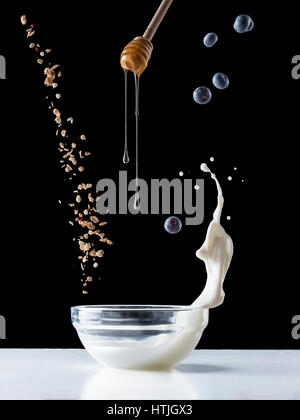 Fallende Müsli mit Milch Spritzen, Heidelbeeren und Honig fließt vom Wagen fallen. Gesundes Frühstückszutaten. Fliegendes Essen Stockfoto