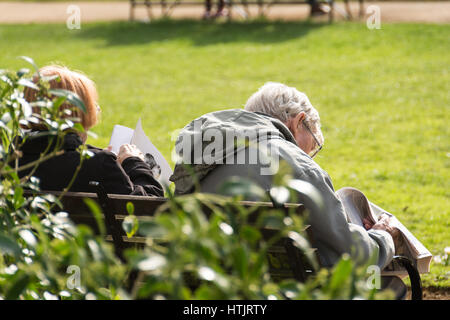 Ein Alter Mann sitzt auf einer Parkbank, lesen eine Zeitung, in der Frühlingssonne am Gordon Square, London, UK Stockfoto