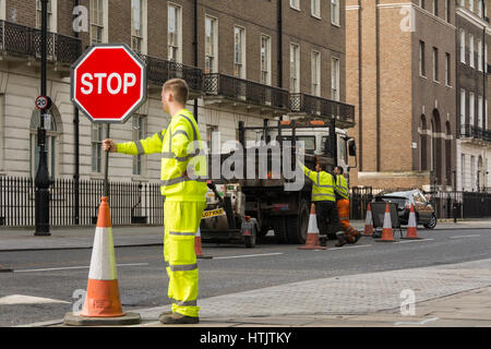 Ein knallfarbener Arbeiter in hoher Kleidung, der den Verkehr lenkt An einem ruhigen London Square Stockfoto