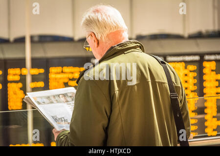 Ein älterer Mann liest Zeitung, während Sie auf einen Zug warten Stockfoto