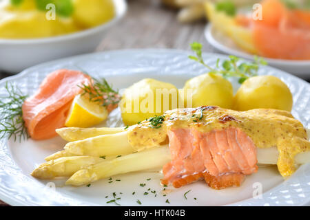 Überbacken weißen Spargel mit geräuchertem Lachs und Käse Soße, serviert mit Salzkartoffeln und Zitrone Stockfoto