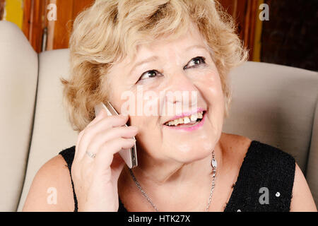 Porträt einer alten Frau am Telefon zu sprechen und auf Couch sitzen. Im Innenbereich. Stockfoto