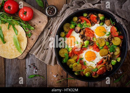 Frühstück für zwei Personen. Spiegeleier mit Gemüse - Shakshuka in einer Pfanne auf einem hölzernen Hintergrund im rustikalen Stil. Flach zu legen. Ansicht von oben Stockfoto