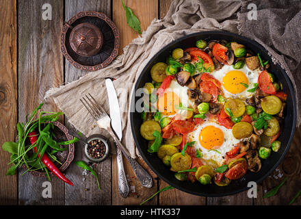 Frühstück für zwei Personen. Spiegeleier mit Gemüse - Shakshuka in einer Pfanne auf einem hölzernen Hintergrund im rustikalen Stil. Flach zu legen. Ansicht von oben Stockfoto