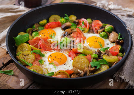 Frühstück für zwei Personen. Spiegeleier mit Gemüse - Shakshuka in einer Pfanne auf einem hölzernen Hintergrund im rustikalen Stil. Stockfoto