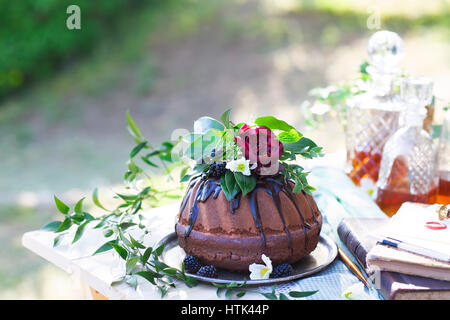 Cocolate Kuchen verziert mit Blumen und drei Whiskey Dekanter gegen einen hellgrauen Hintergrund mit Textfreiraum Stockfoto