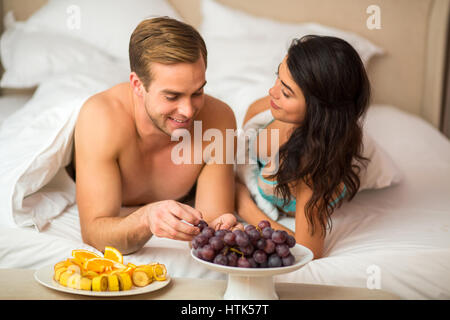 Paar mit Früchten im Bett. In Scheiben geschnittenen Bananen und Trauben. Perfekte Rezept der Romantik. Stockfoto