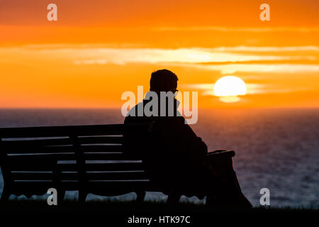 Aberystwyth Wales UK, Sonntag 12. März 2017 UK Wetter: ein Mann sitzt allein und starrt auf die untergehende Sonne spektakulär über den Wassern der Cardigan Bay aus Aberystwyth an der Westküste von Wales. Foto Credit: Keith Morris/Alamy Live-Nachrichten Stockfoto