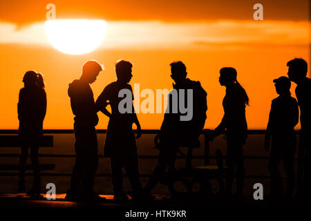 Aberystwyth Wales UK, Sonntag 12. März 2017 UK Wetter: eine Gruppe von Menschen gefangen in der Silhouette als hinter ihnen die Sonne spektakulär über den Wassern der Cardigan Bay aus Aberystwyth an der Westküste von Wales untergeht. Foto Credit: Keith Morris/Alamy Live-Nachrichten Stockfoto