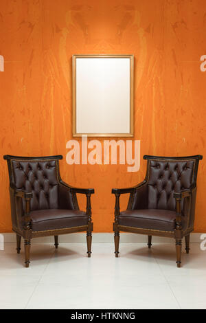 Zwei leere Stühle in einem Wohnzimmer mit Orange Wand Hintergrund Stockfoto