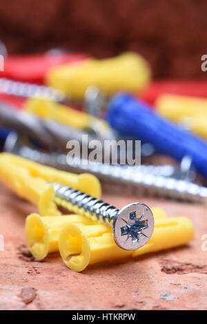 Plasctic Dübel Schrauben und Werkzeug auf Ziegel Hintergrund Nahaufnahme Stockfoto