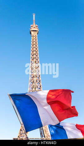 Eine französische Flagge fliegt vor dem Eiffelturm in Paris Frankreich an einem Tag blauer Himmel. Stockfoto