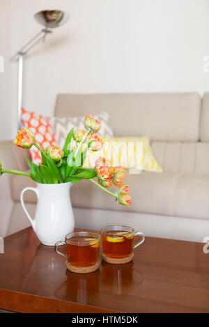 Schöne orange Tulpen Bukett mit zwei Tassen Tee auf Holztisch im Wohnzimmer Stockfoto