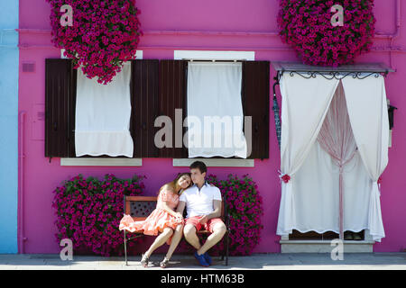 Jung Reisen paar im Urlaub entspannen Sie sich auf eine Bank in der Nähe von einem lila Haus in Burano, Venedig, Italien Stockfoto