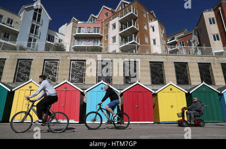 Menschen machen ihren Weg vorbei an bunten Beach an Boscombe Strand in Bournemouth, Dorset, Hütten, wie eines der wärmsten Tage des Jahres so weit mit Feder heute etwas mehr als eine Woche Weg sein könnte. Stockfoto