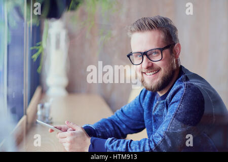 Ein freier Hipster-Mann mit Tablet in der Hand arbeitet Café am Fenster. Stockfoto