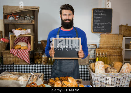 Porträt von männlichen Personal holding Board mit Schild am Zähler in Bäckerei öffnen Stockfoto