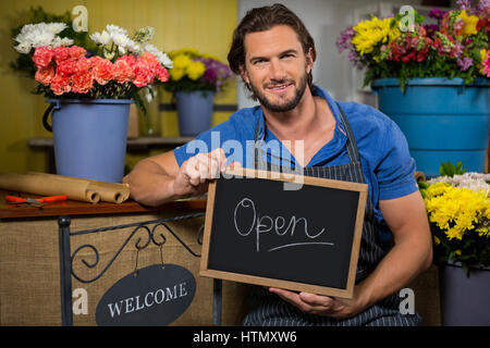 Porträt der männlichen Angestellten halten ein Brett mit Schild "geöffnet" in Blumenladen Stockfoto