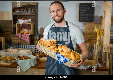 Lächelnd männliche Angestellten halten Weidenkorb an verschiedenen Brotsorten am Schalter in Bäckerei Stockfoto