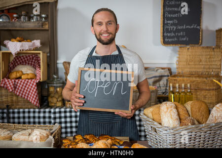 Porträt von lächelnden Personal holding Tafel mit Zeichen am Schalter in Bäckerei öffnen Stockfoto