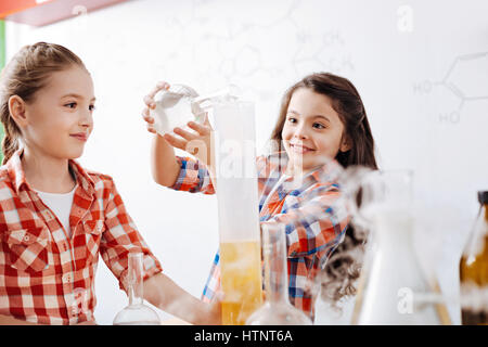 Kleine Forscher. Fröhliche helle hübsches Mädchen hält eine Flasche und Gießen eine chemische Flüssigkeit beim Experimentieren im Labor Stockfoto