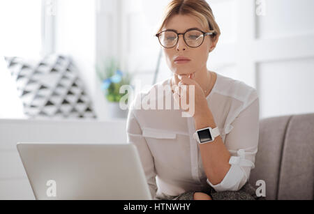 Erfolgreiche Frauen. Nette attraktive nachdenklich Geschäftsfrau trägt Brille und hält ihr Kinn beim Betrachten der Laptop-Bildschirm Stockfoto