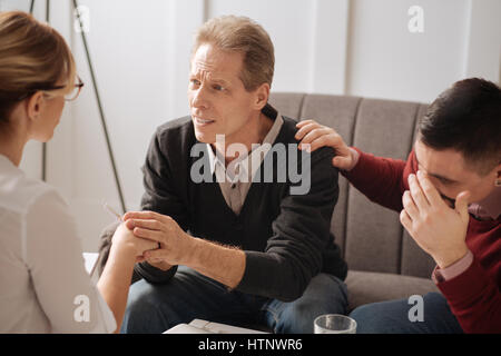 Helfen Sie uns. Netter hoffnungsvoll angenehmen Mann hält eine Hand des Therapeuten und sah sie beim bitten um Ratschlag Stockfoto