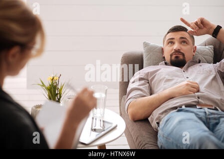 Psychologische Behandlung. Schöne nachdenkliche bärtiger Mann auf dem Sofa liegen und versuchen zu entspannen während des Besuchs eines Psychologen Stockfoto