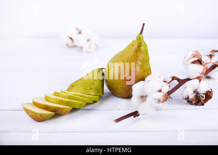 frische reifer BIO Birne auf weißem Holz Hintergrund mit Baumwollblume und eine andere Birne in Stücke geschnitten. Hohen Schlüsselfoto. Stockfoto