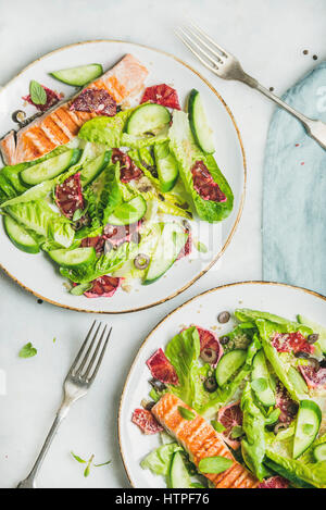 Gesunde Energie fördernde Frühlingssalat mit gegrillten Lachs, Blutorange, Oliven, Gurken und Quinoa, Draufsicht, Marmor Hintergrund. Sauber, Essen, dietin Stockfoto