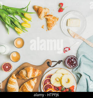 Frühstück mit Croissants, Butter, Himbeer Marmelade, frisches Obst, Milch in der Flasche, Kaffee Espresso und gelbe Tulpe Frühlingsblumen. Ansicht von oben, Kopie s Stockfoto