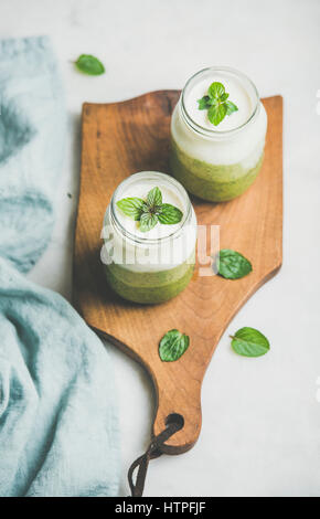 Ombre grüne Smoothies mit Minze im Glas auf Holzbrett über hellen grauen Hintergrund, selektiven Fokus geschichtet. Essen, Vegan, vegetarisch, reinigen wir Stockfoto