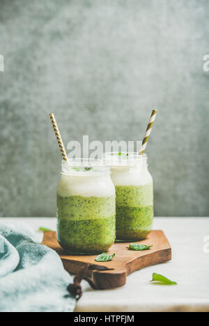 Ombre geschichteten grüne Smoothies mit Minze im Glas mit einem Strohhalm auf Holzbrett, graue Betonwand Hintergrund, Textfreiraum, selektiven Fokus. Sauber e Stockfoto