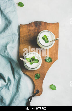 Ombre grüne Smoothies mit Minze im Glas mit einem Strohhalm auf Holzbrett über hellen grauen Hintergrund, Draufsicht geschichtet. Essen, Vegan, versammelt zu reinigen Stockfoto